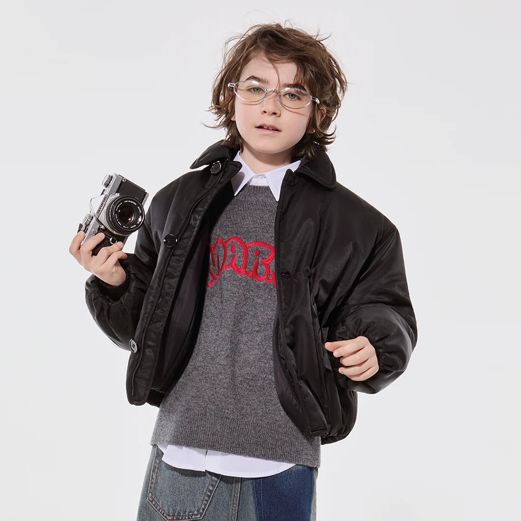 Boy wearing a stylish casual outfit with a bomber jacket, holding a camera on a neutral background.