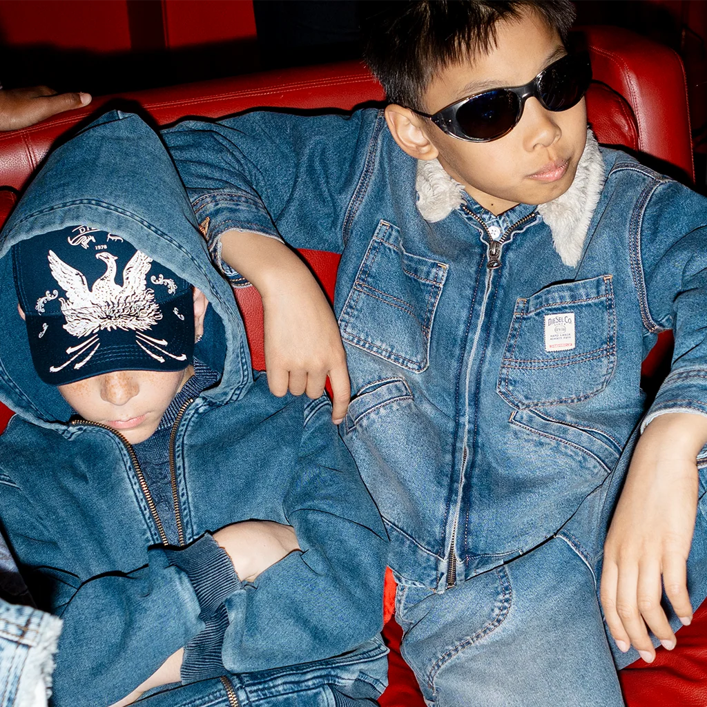 Two boys lying on a red couch and wearing total denim outfits.