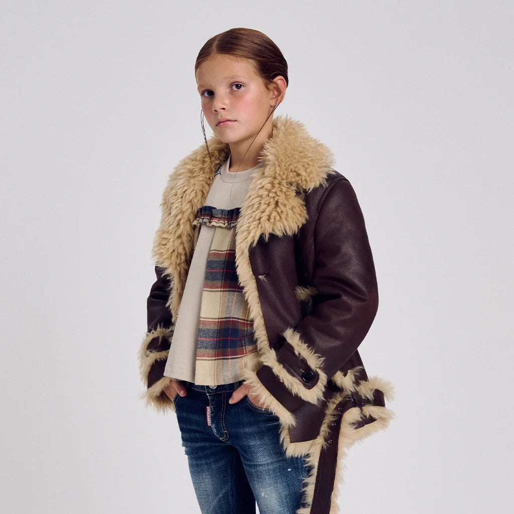 A child model wearing a warm leather jacket, a checked shirt and a pair of jeans..