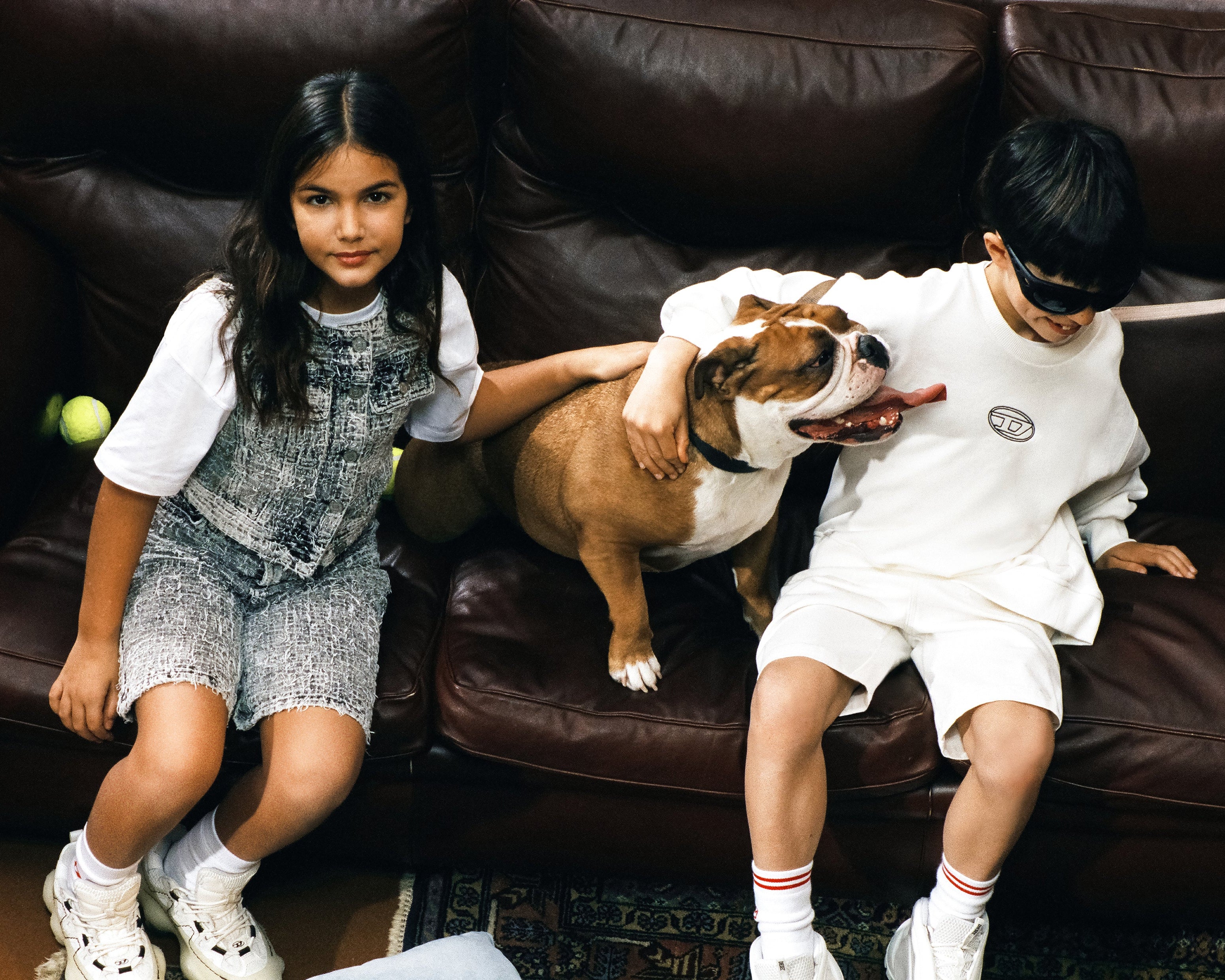 Two children sitting on a brown leather couch with a dog.