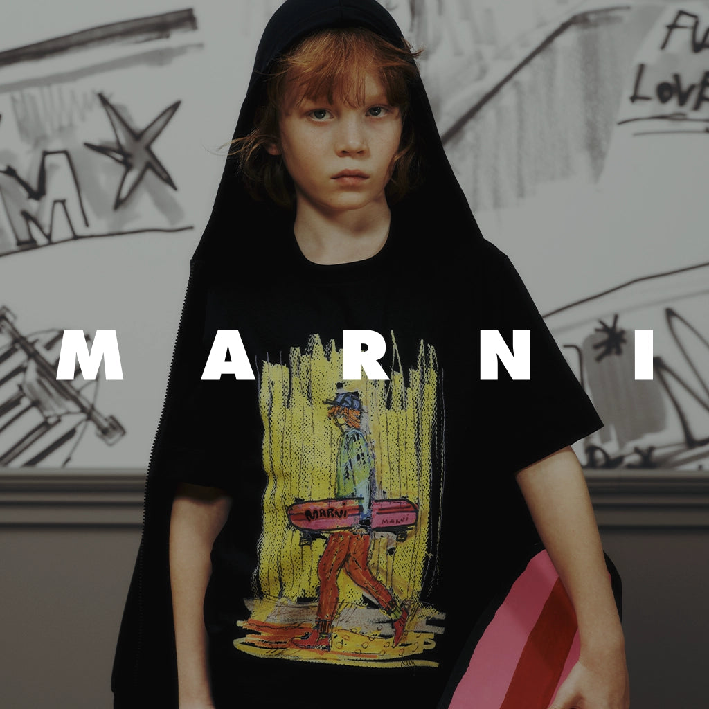 A child wearing a black T-shirt with a colorful graphic print and large white 'MARNI' lettering across the front, posed indoors against a sketchy wall.